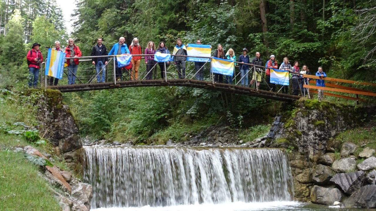 Ein Teil der Mitglieder der Klimagruppe Simme - Saane stehen auf einer Brücke mit der Fahne der Gletscher-Initiative.